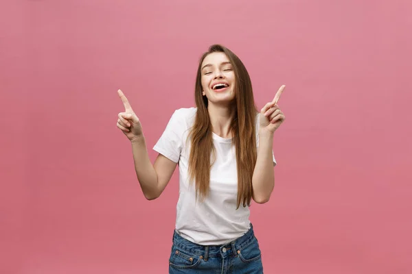 Φωτογραφία της χαρούμενης νεαρής γυναίκας στέκεται και poiting δάχτυλο απομονώνονται σε ροζ φόντο. — Φωτογραφία Αρχείου