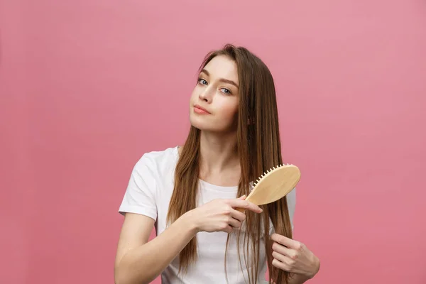 Wanita muda tersenyum menyisir rambut dan memandang jauh terisolasi di merah muda — Stok Foto