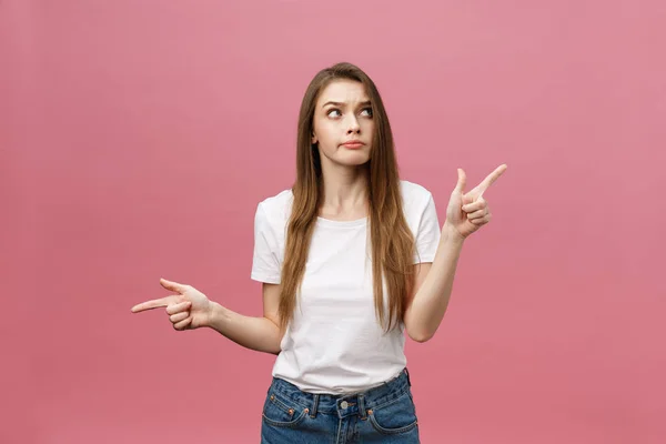 Closeup of serious strict young woman wears white shirt looks stressed and pointing up with finger isolated over pink background — Stock Photo, Image