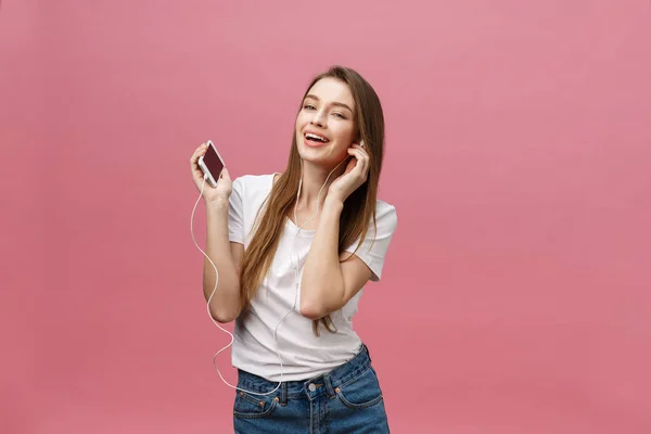 Concepto de estilo de vida. Mujer joven usando el teléfono para escuchar música sobre fondo rosa — Foto de Stock