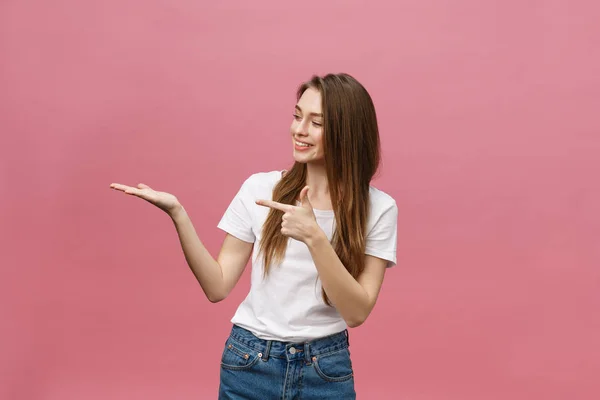 Молодая девушка в белой рубашке указывая стороны, чтобы представить продукт на изолированном розовом фоне — стоковое фото