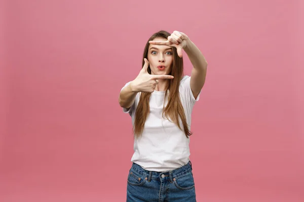見てみるとビックリ、口を大きく開いて、維持する陽気な若い女性は、明るいピンクの背景に分離された手フォト フレーム ジェスチャーを作る. — ストック写真