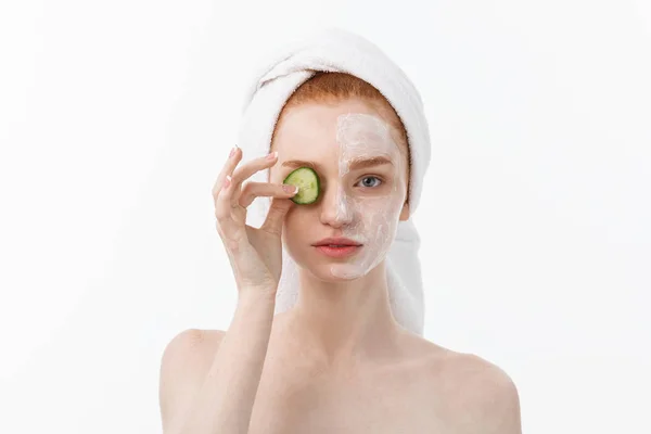 Vonzó fiatal nő szép tiszta bőr. Fehér maszkot, és uborka. Kozmetikai kezelések és kozmetológiai spa kezelés. Fehér háttér — Stock Fotó