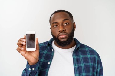 Yakışıklı Afrikalı adam gri arka planda izole, akıllı telefon sunan ve boş siyah ekranda parmak ile işaret.