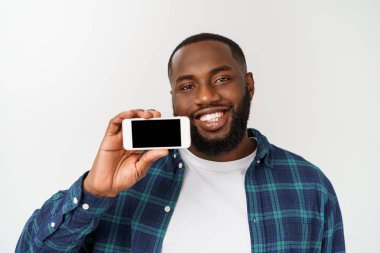 Yakışıklı Afrikalı adam gri arka planda izole, akıllı telefon sunan ve boş siyah ekranda parmak ile işaret.