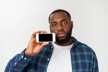 Yakışıklı Afrikalı adam gri arka planda izole, akıllı telefon sunan ve boş siyah ekranda parmak ile işaret.