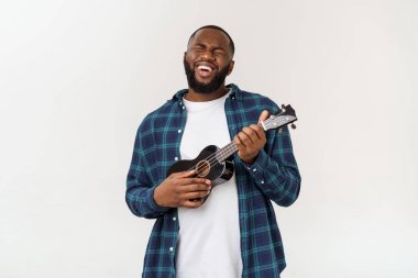 Genç ve yakışıklı Afro-Amerikan adam beyaz arka planda ukulele çalıyor.,