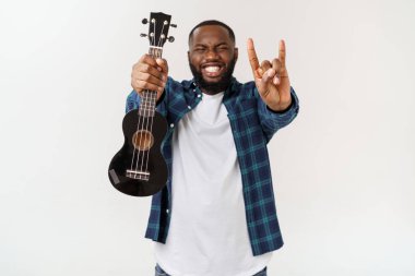 Genç ve yakışıklı Afro-Amerikan adam beyaz arka planda ukulele çalıyor.,