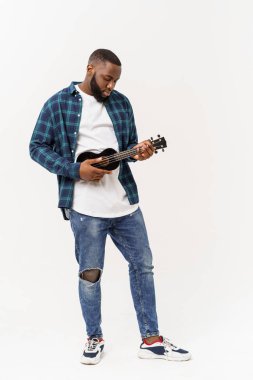 Genç ve yakışıklı Afro-Amerikan adam beyaz arka planda ukulele çalıyor.,