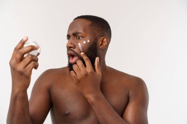 Yüzünde krem uygulayarak gülümseyen Afro adam. Mans Cilt Bakımı kavramı