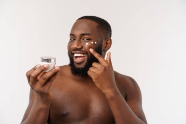 Yüzünde krem uygulayarak gülümseyen Afro adam. Mans Cilt Bakımı kavramı