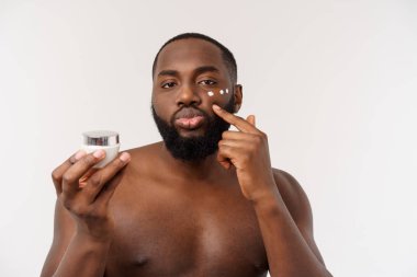 Yüzünde krem uygulayarak gülümseyen Afro adam. Mans Cilt Bakımı kavramı