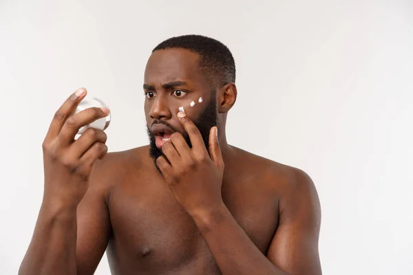 Sonriente afro-hombre aplicándose crema en la cara. Concepto para el cuidado de la piel —  Fotos de Stock