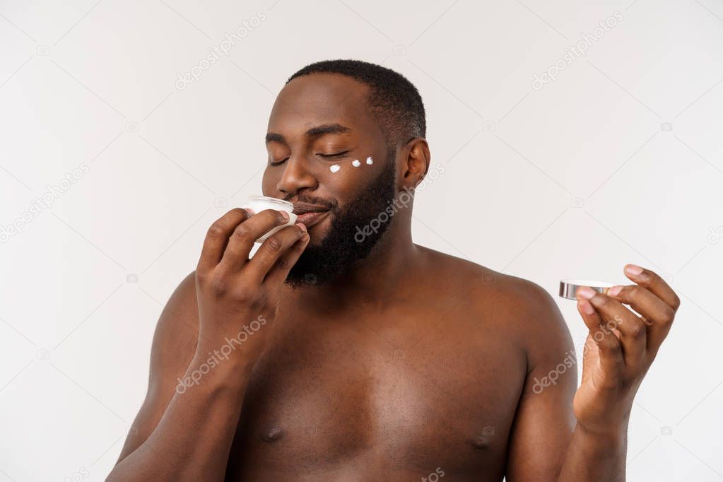 Smiling afro man applying cream on his face. Mans skin care concept