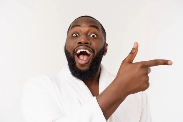 Pria kulit hitam mengenakan jubah mandi menunjuk jari dengan kejutan dan emosi bahagia. Terisolasi di atas latar belakang whtie . — Stok Foto
