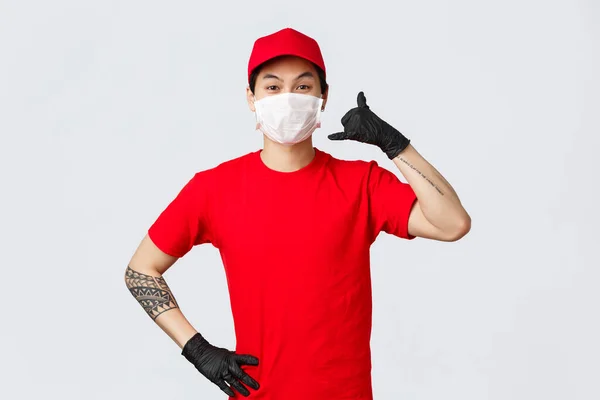 Vrolijke aziatische bezorger met medisch masker en beschermende handschoenen tonen telefoon teken, vragen klanten bellen wanneer de levering nodig is. Charismatische koerier bevorderen snelle verzending van pakket — Stockfoto