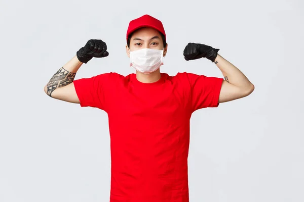 Silný sebevědomý asijský poslíček, ohebný biceps, s lékařskou maskou a ochrannými rukavicemi. Reklama na bezpečné a rychlé kurýrní služby během pandemické covid 19 self-izolace — Stock fotografie
