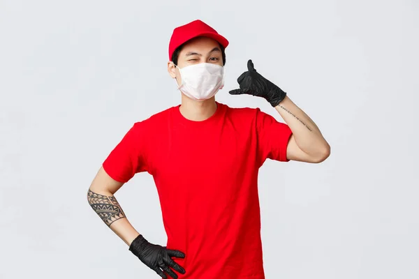 Happy asian delivery guy in medical mask tell give call, wink cheeky to client, keep in touch when delivery needed, fast shipment, good quality of courier services, safe shopping during pandemic