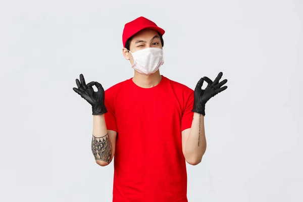 Keep calm and rely on our deliver company. Cheerful relaxed asian delivery guy in red cap and t-shirt, show zen, nirvana gesture and wink, assure your package safe. Courier stay peaceful — Stock Photo, Image