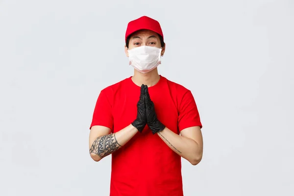 S'il vous plaît rester en sécurité à la maison, nous livrons vos commandes. mignon asiatique livraison guy en rouge cap et t-shirt, portant masque de protection et gants, montrer les mains dans prier, mendier, plaider pour quelque chose — Photo