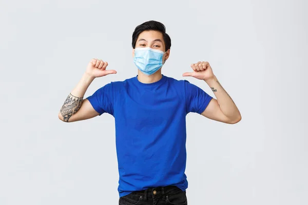 Olika känslor, social distans, självkarantän på coronavirus och livsstil koncept. Självsäker leende asiatisk man i medicinsk mask, pekar sig med stolt uttryck, skryta eller skryta — Stockfoto