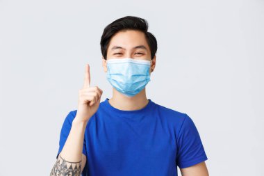 Coronavirus sırasında farklı duygular, yaşam tarzı ve rahatlık, covid-19 konsepti. Tıbbi maskeli mutlu Asyalı genç adamın yakın plan, makyaj fikri ya da çözümü için işaret parmağını kaldırması.