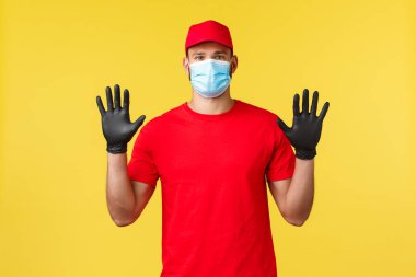 Salgın sırasında hızlı teslimat, covid-19, güvenli nakliye, online alışveriş konsepti. Kırmızı üniformalı genç kurye, koruyucu tıbbi maske eldivenli temiz elleri gösteriyor, çalışan posta dağıtıyor.