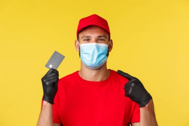 Covid-19, teslimat emirleri, alışveriş, temassız ödeme ve sosyal uzaklık konsepti. Hoş kuryeye yakın plan, kırmızı üniformalı erkek çalışan, kredi kartını işaret eden.