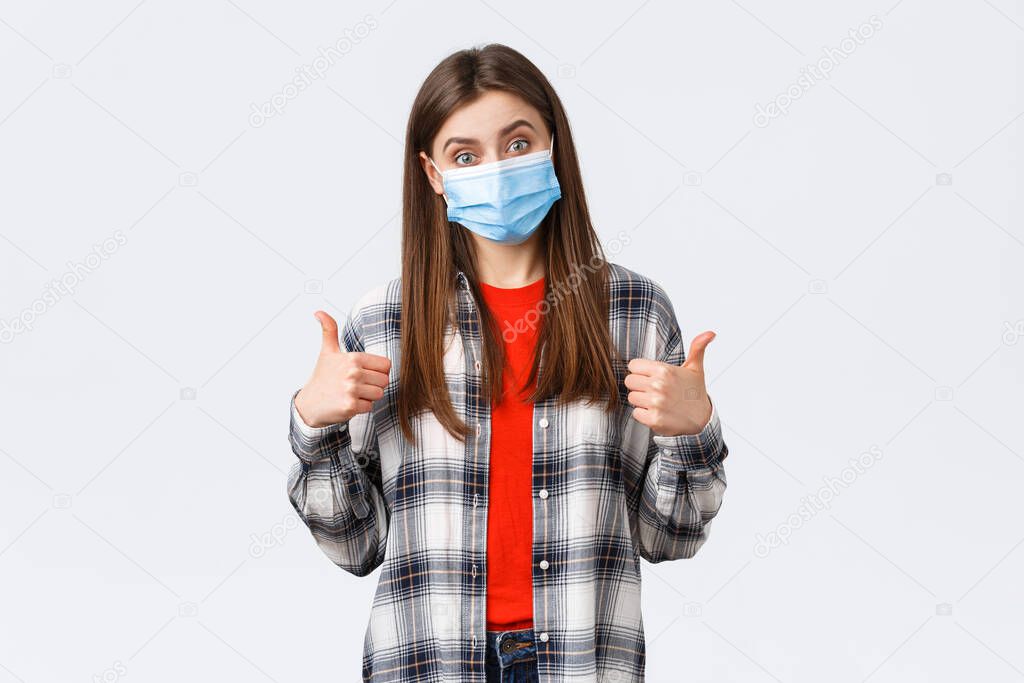 Coronavirus outbreak, leisure on quarantine, social distancing and emotions concept. Very good congratulations. Supportive cute woman in medical mask show thumb-up, like and approve