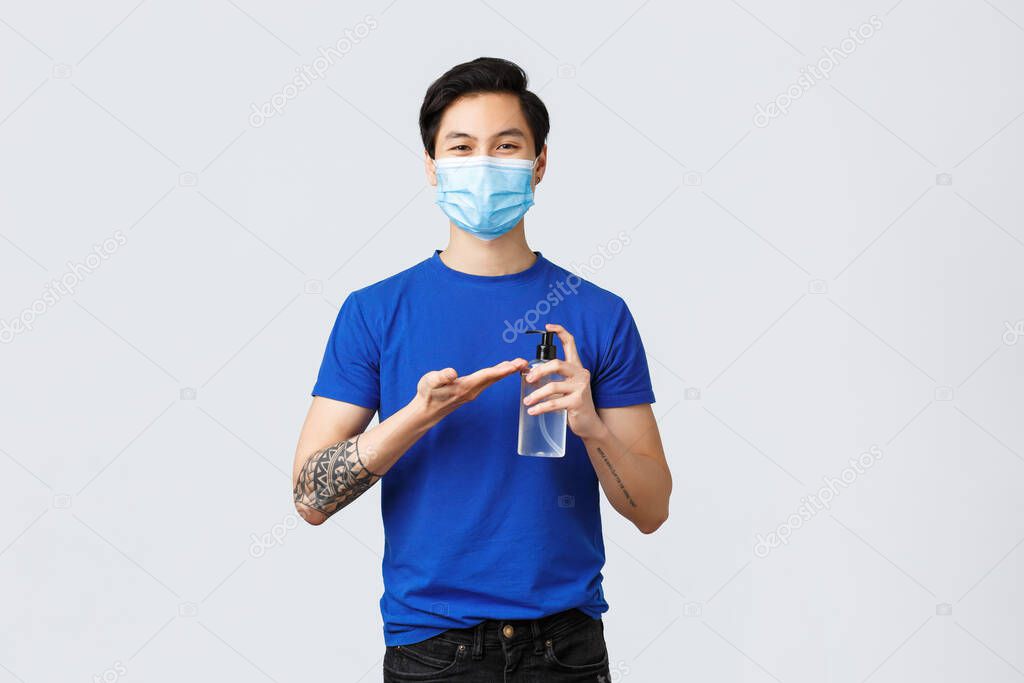 Lifestyle, people different emotions and covid-19 pandemic concept. Smiling handsome asian man in medical mask apply hand sanitizer on hand to stay safe from virus spread