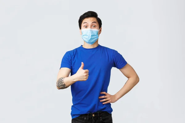 Different emotions, social distancing, self-quarantine on covid-19 and lifestyle concept. Surprised and impressed supportive asian guy thumbs-up to good idea, wearing medical mask — Stock Photo, Image