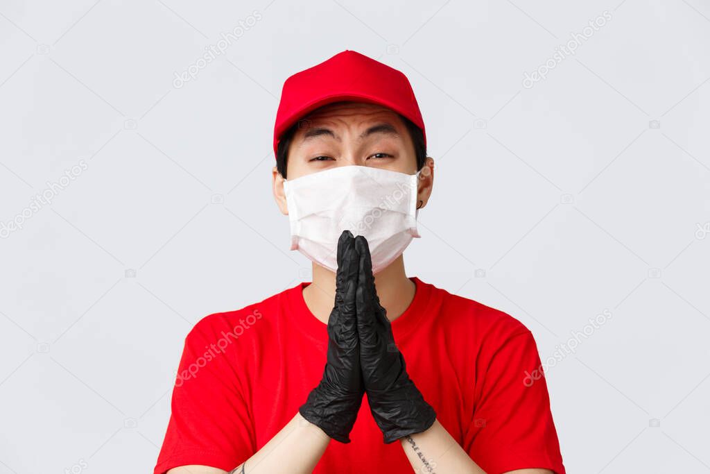 Covid-19, self-quarantine online shopping and delivery concept. Clingy asian courier in medical mask and gloves, begging for favour, pleading for favour, need help, standing grey background