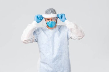 Covid-19 salgını, virüs salgını, klinik ve sağlık çalışanları konsepti. Kendine güvenen genç doktor, profesyonel koronavirüs salgını, yüz kalkanı ve kişisel koruyucu ekipman takıldı.