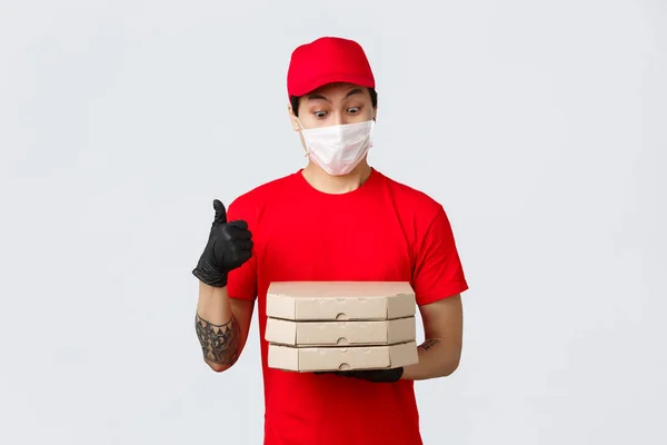 Amazed asiatico ragazzo consegna cant resistere tentazione odore gustosa pizza in scatole, spettacolo pollice in su. Courier consiglia app per l'ordine di cibo durante la quarantena. Stai al sicuro e mangia a casa. — Foto Stock