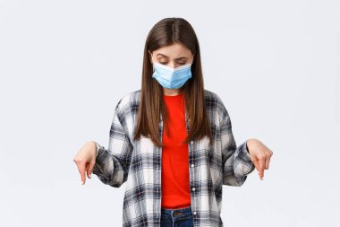 Coronavirus salgını, karantina, sosyal mesafeler ve duygu kavramı. Tereddütlü ve kararsız tıbbi maskeli çekici kadın, aşağıya bakıyor, garip bir şeyi işaret ediyor.