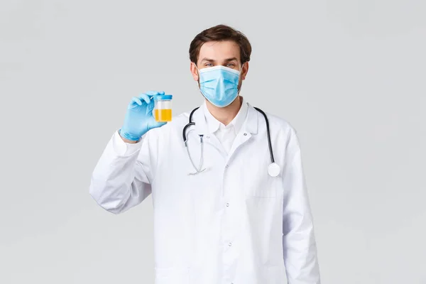 Hôpital, travailleurs de la santé, concept de traitement covid-19. Médecin optimiste souriant dans les blouses blanches, porter des mas médicaux et des gants, technicien de laboratoire montrant récipient avec échantillon d'urine — Photo