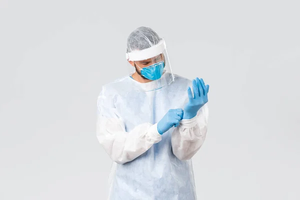 Pandemia de Covid-19, brote de virus, concepto de trabajadores de la salud. Médico profesional serio en equipo de protección personal poner guantes de goma, entrar en la sala de la clínica con pacientes infecciosos coronavirus — Foto de Stock