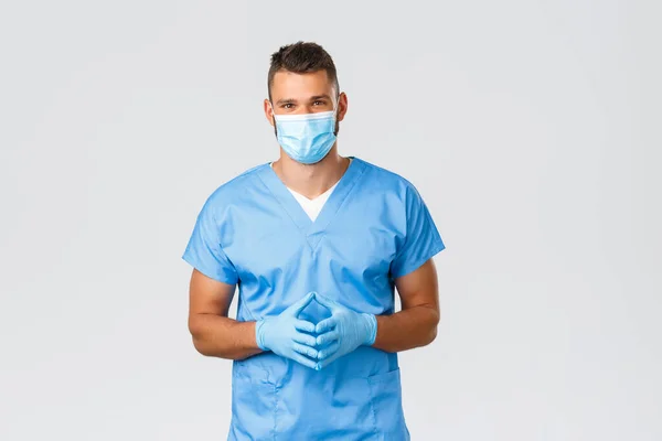 Gezondheidswerkers, covid-19, coronavirus en het voorkomen van virus concept. Vriendelijk knappe arts, verpleegkundige in scrubs en medisch masker, luisteren naar de patiënt tijdens casual screening, grijze achtergrond — Stockfoto