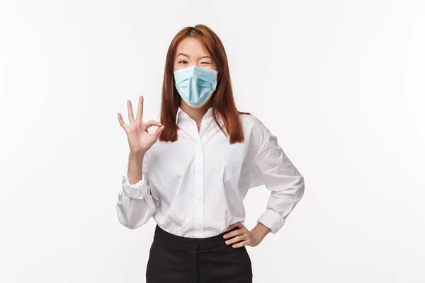 Unbothered cheerful pretty asian woman in white shirt, show okay gesture, confirm work done, wink and smiling happy, assure all good, everything perfect, excellent job, white background — Stock Photo, Image