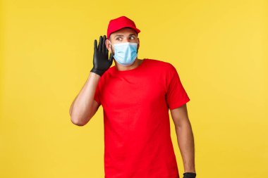 Salgın sırasında hızlı teslimat, covid-19, güvenli nakliye, online alışveriş konsepti. Kırmızı üniformalı ve tıbbi maskeli kurye heyecanlı ve ilgili, el ele tutuşun ve kulak misafiri olun.