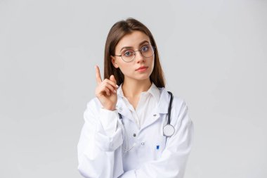 Sağlık çalışanları, ilaç, sigorta ve covid-19 salgını konsepti. Beyaz önlüklü, gözlüklü, akıllı, profesyonel kadın doktor. Fikri olan, önerisi olan, işaret parmağını kaldıran.