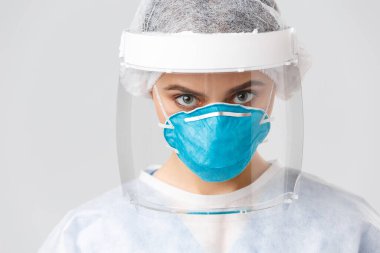 Covid-19, virüsü önleme, sağlık çalışanları ve karantina konsepti. Kişisel koruyucu kostüm, solunum cihazı ve yüz kalkanı takmış ciddi, kararlı bir doktor ya da hemşireye yakın çekim.