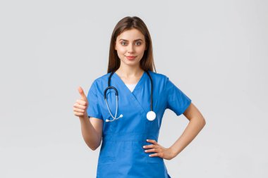 Tıp çalışanları, covid-19 ve aşı konsepti. Kendine güvenen profesyonel doktor, mavi önlüklü ve steteskoplu bayan hemşire, baş parmaklarınızı kaldırın, klinikteki en iyi hizmeti sağlayın veya garanti edin.