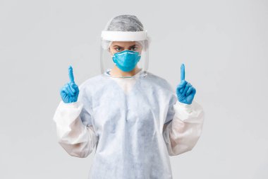 Covid-19, virüsün önlenmesi, sağlık, sağlık çalışanları ve karantina konsepti. Hasta Coronavirüs hastalarıyla çalışan kararlı genç bir doktor ya da hemşire. Parmakla işaret ediyor, koruyucu elbise giyiyor.