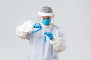 Covid-19, tıbbi araştırma, sağlık çalışanları ve karantina konsepti. Klinikteki teknoloji laboratuarı doktoru Coronavirus aşısı üzerinde çalışıyor, başka bir test tüpüne sıvı dolduruyor, kişisel koruyucu kostüm giyiyor.