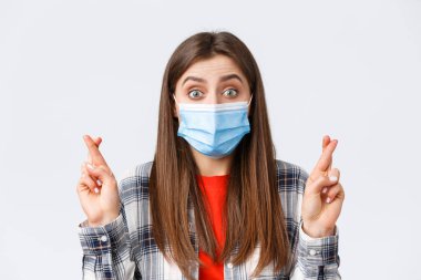 Coronavirus salgını, karantina, sosyal mesafeler ve duygu kavramı. Umut dolu, tıbbi maskeli güzel bir kız, iyi haberler bekliyor, rüyaların gerçek olduğuna inanıyor, dilek tutarken şans diliyor.