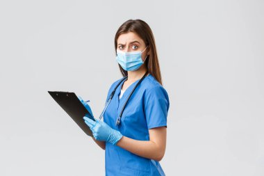 Covid-19, virüsün önlenmesi, sağlık, sağlık çalışanları ve karantina konsepti. Şüpheci ve şüpheci bayan hemşire, mavi önlüklü doktor hasta formlarını doldurup panoda kamerayı şaşırttı.