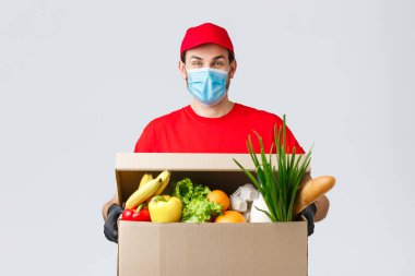 Erzak ve paket teslimatı, covid-19, karantina ve alışveriş konsepti. Yüz maskeli ve eldivenli arkadaş canlısı kurye Coronavirus sırasında müşterilerin evine yiyecek götürüyordu.