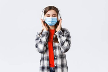 Sosyal uzaklık, rahatlık ve covid-19 'da yaşam tarzı, koronavirüs konsepti. Dertsiz, rahat, tıbbi maskeli bir kadın kulaklıkla müzik dinliyor, gözlerini kapatıyor.