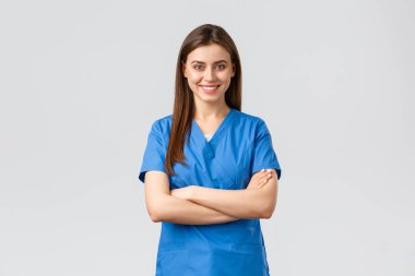 Sağlık çalışanları, virüsü, sigortayı ve ilaç konseptini engelleyin. Kendine güvenen kadın doktor, mavi önlüklü hemşire, gülümseyen ve çapraz kollu göğüs, hastanın hayatını kurtarmaya hazır, gri arka plan.